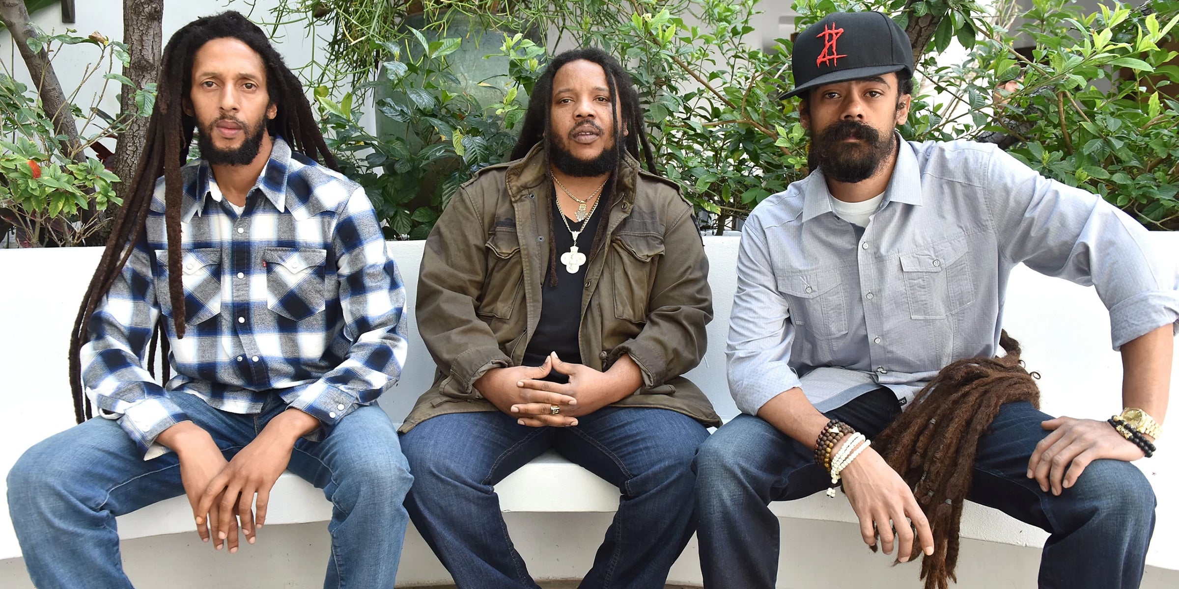 Three men with dreadlocks sitting on a bench outdoors.